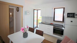 A modern kitchen with white cabinets, a built-in oven, and a microwave. There's a dining table with chairs and a vase of flowers. - Light-filled apartment just 400 metres from the beach with sea views, WiFi, air conditioning (Porec)