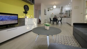 Een moderne woonkamer met een flatscreen televisie, een ronde salontafel met planten, een bank en een eethoek met een tafel en stoelen.