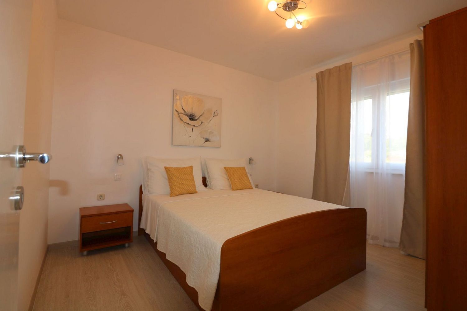 A bedroom with a wooden bed, a nightstand, a painting on the wall, and a window with curtains.