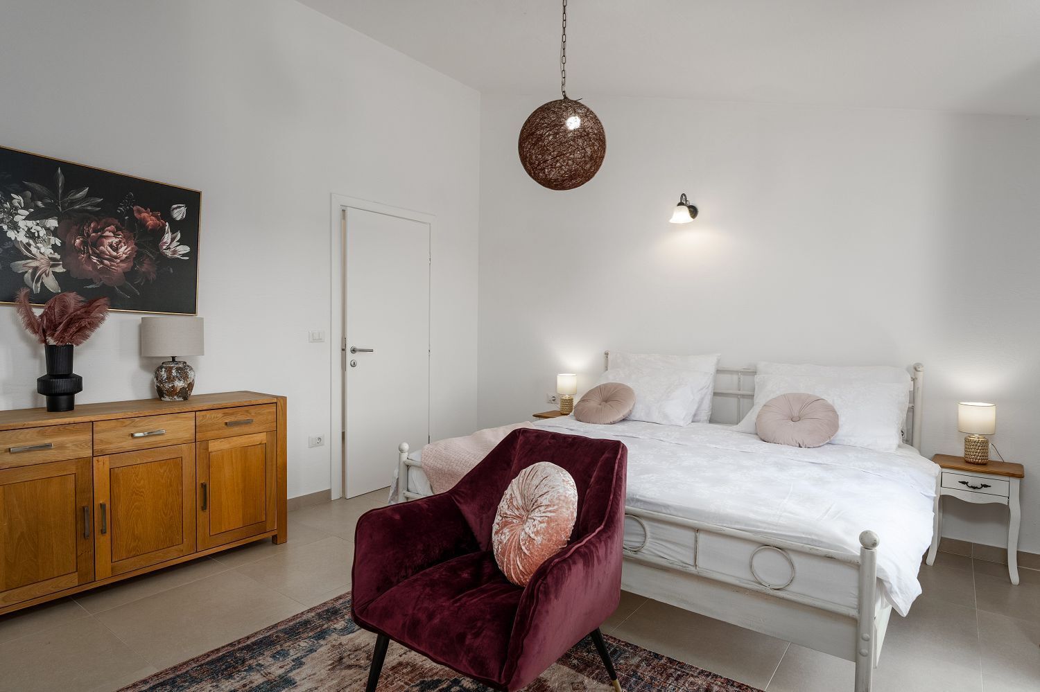 A bedroom with a bed, bedside tables, a chair, a wardrobe, and a hanging light fixture.