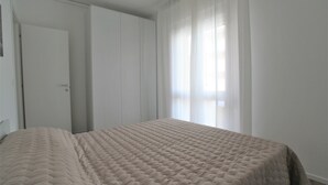 A bedroom with a bed, a door, and a window with sheer curtains. - Cozy Apartment With Balcony Near Piazza Torino (Jesolo)