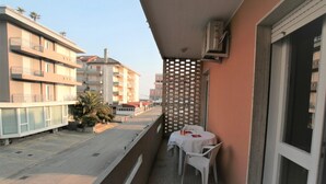 A balcony with a table and chairs, a lattice partition, and a view of surrounding buildings. - Cozy Apartment With Balcony Near Piazza Torino (Jesolo)