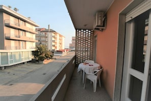 Ein Balkon mit Tisch und Stühlen, einem Gitterzaun und Blick auf umliegende Gebäude.