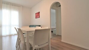 A dining area with a white table and chairs, a sign on the wall, and a doorway leading to another room. - Cozy Apartment With Balcony Near Piazza Torino (Jesolo)
