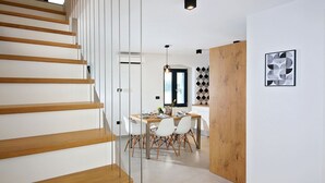 Een modern interieur met een houten trap, een eethoek met witte stoelen en een geometrisch patroon op de muur.