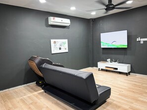 A modern room with a reclining chair, a flat-screen TV, a ceiling fan, and a mounted air conditioner.