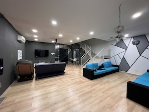 A modern living room with a sofa, a coffee table, and a TV mounted on the wall. There is a staircase leading to another level. - Spacious 4-bedroom house in enchanting Melaka with AC comfort (Melaka)
