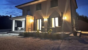 Una casa moderna de dos pisos con un porche cubierto, mobiliario exterior y una entrada bien iluminada.