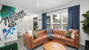 En moderne stue med en hjørnesofa, et rundt sofabord og en trappe til et andet niveau.