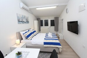 Kompakti hotellihuone, jossa on sänky, yöpöytä, televisio ja pieni työpöytä.