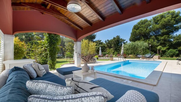 Un espacio de estar al aire libre cubierto con piscina, sillones de descanso y una pérgola.