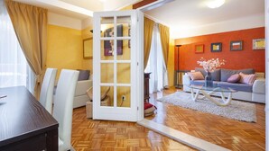 Una sala de estar moderna con piso de madera en espiga, una mesa de centro de vidrio, un sofá y un comedor con mesa y sillas.