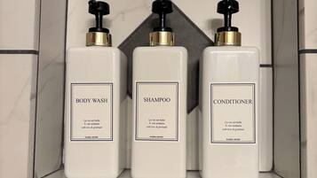 Three white bottles of body wash, shampoo, and conditioner in a tiled bathroom shelf.