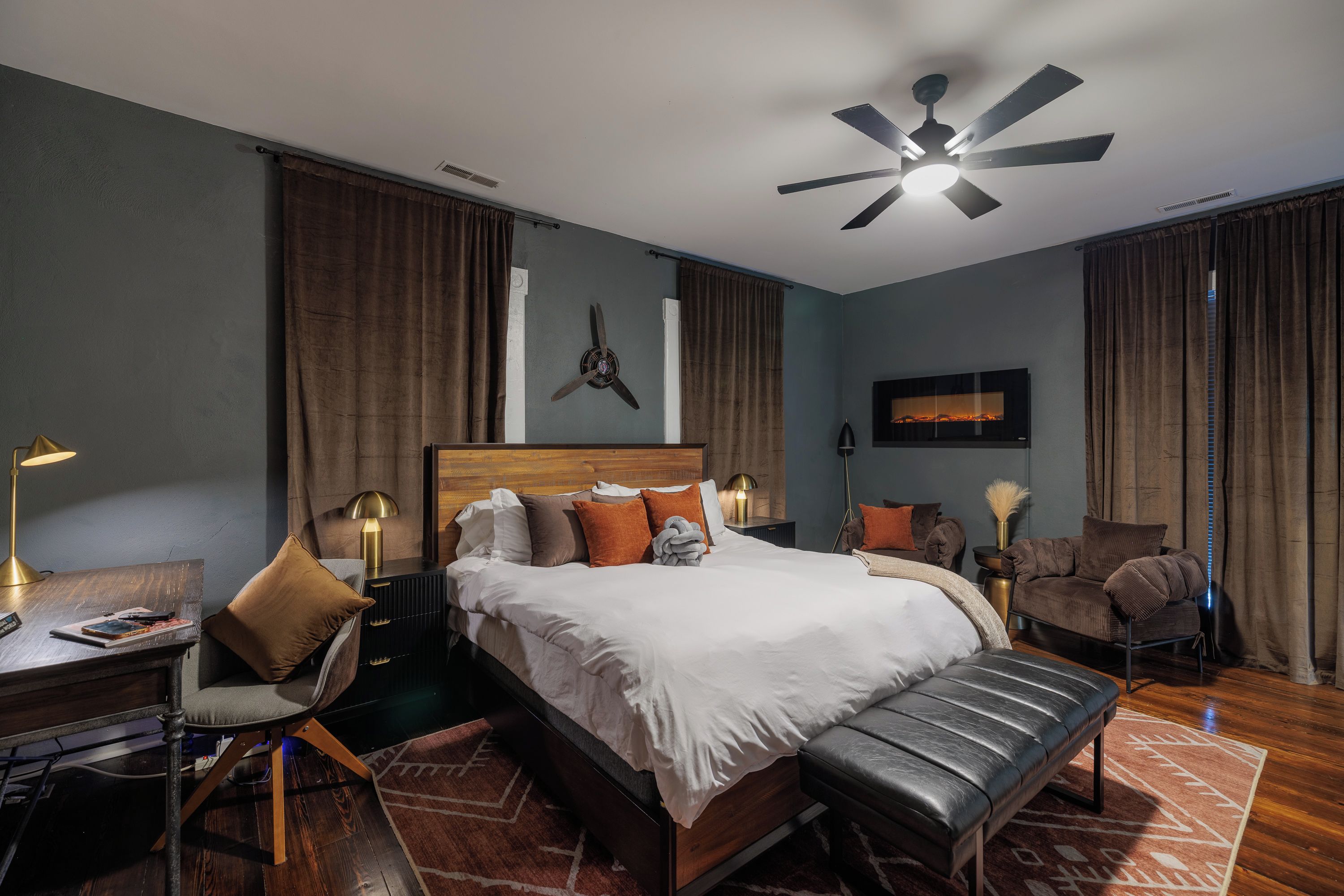 Une chambre d’hôtel moderne dotée d’un grand lit, d’un bureau, d’une chaise, d’une banquette, d’un ventilateur de plafond et d’une cheminée.