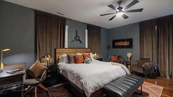 A modern hotel room with a large bed, a desk, a chair, a bench, a ceiling fan, and a fireplace.