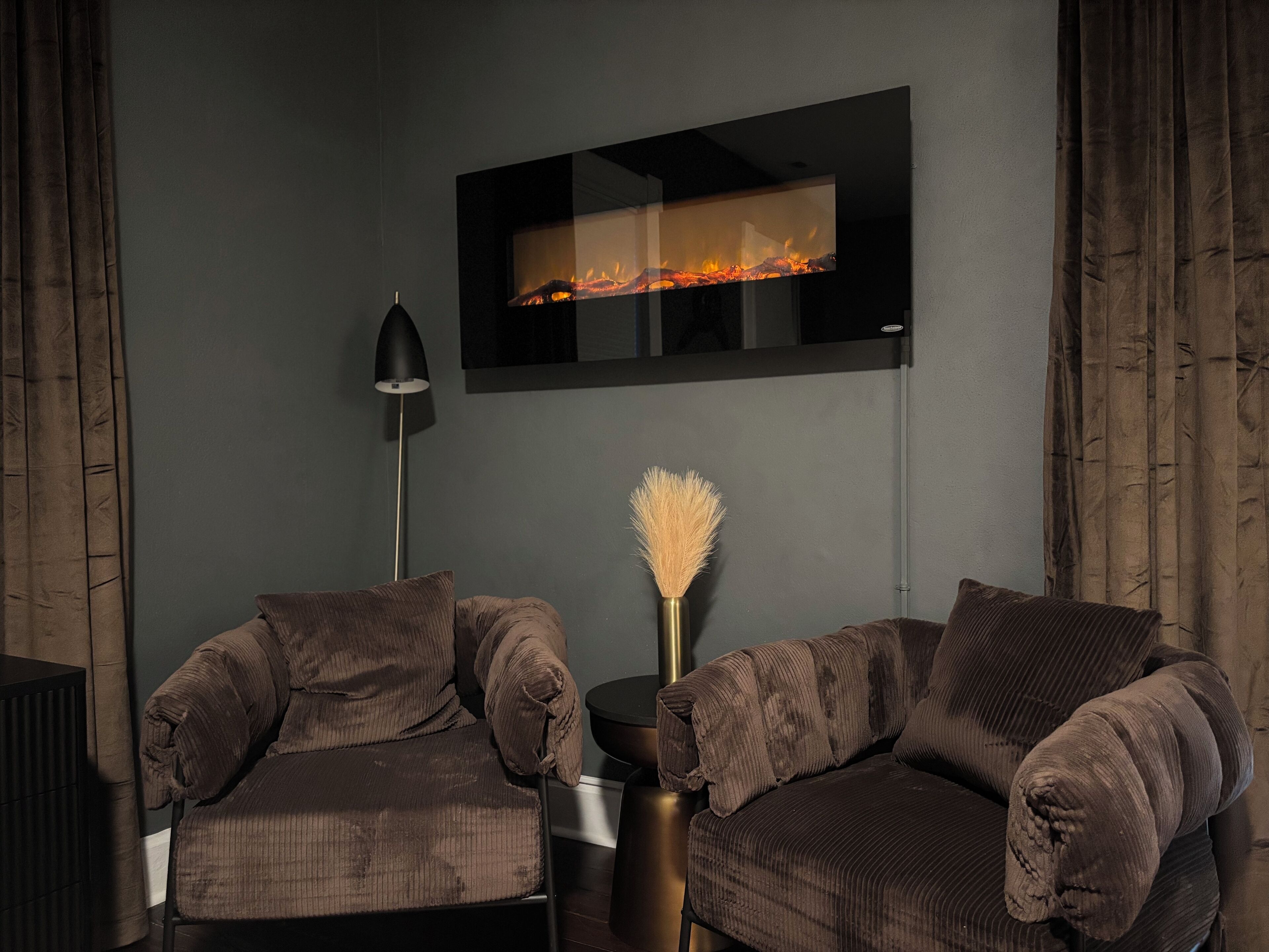 Una sala de estar moderna con chimenea, dos sofás marrones, una lámpara de pie y un florero con una pluma.