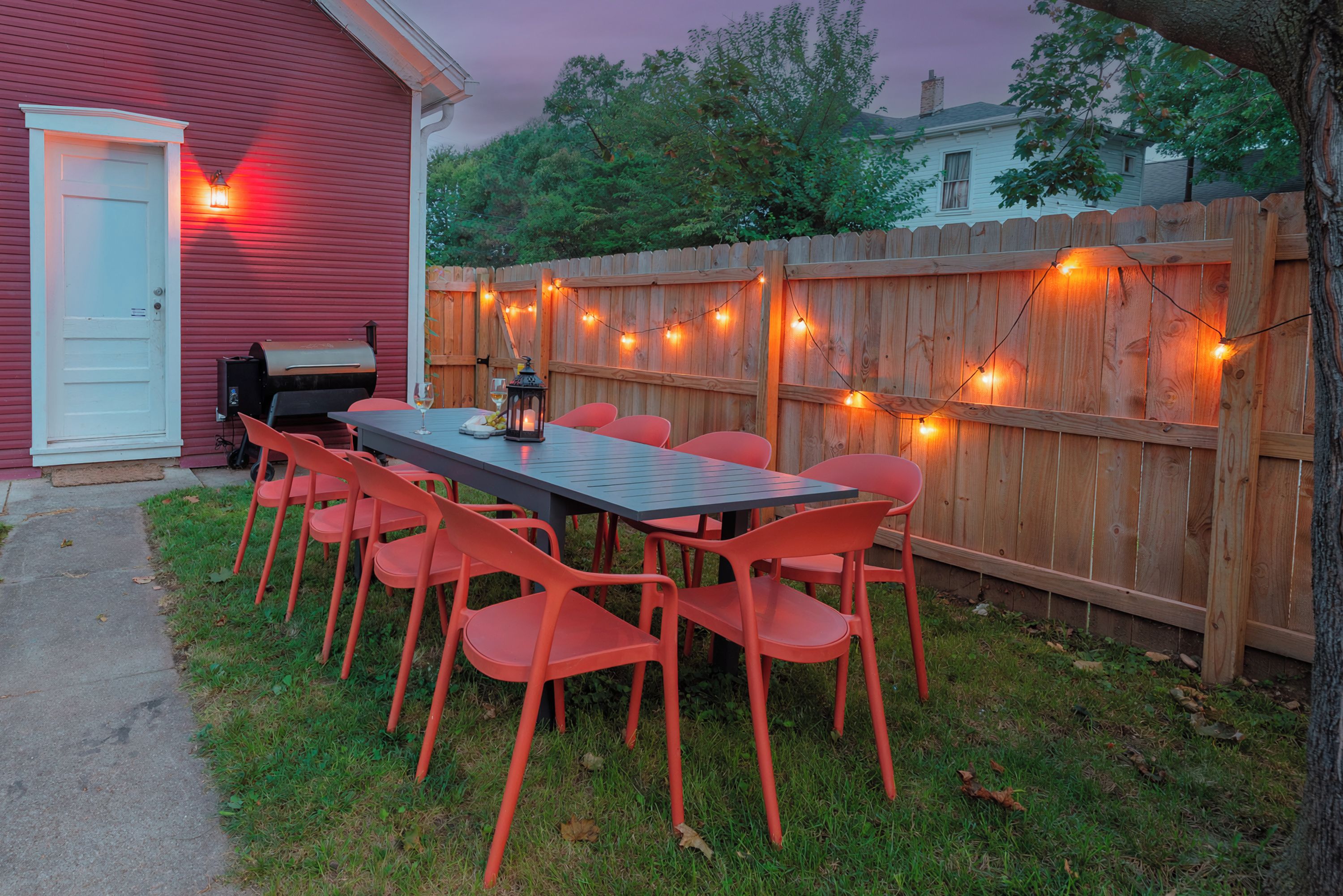 Un patio al aire libre con mesa y sillas, una parrilla y luces colgantes.
