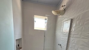 Ett litet, avskilt duschutrymme med ett fönster, en toalett och en handduksställning.