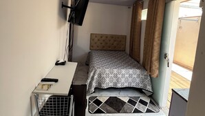 Ett litet sovrum med en säng, ett skrivbord, en stol, en takfläkt och ett fönster med gardiner.