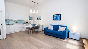 A modern living room with a blue sofa, a dining table with chairs, a kitchen area with white cabinets, and a blue artwork on the wall. - Impressive apartment with sea view right in Rovinj, only 200 metres from the beach (Rovinj)