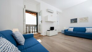 A modern living room with two blue sofas, a white entertainment unit, and a balcony with a view. - Impressive apartment with sea view right in Rovinj, only 200 metres from the beach (Rovinj)