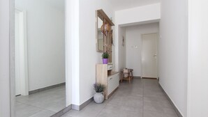 A clean, modern hallway with a wooden bench, a small table, and a potted plant. - Modern apartment with charming terrace, private parking, air conditioning, WiFi (Rovinj)