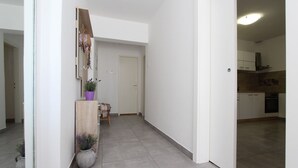 A modern, minimalist hallway with a wooden bench, a potted plant, and a door leading to a kitchen area. - Modern apartment with charming terrace, private parking, air conditioning, WiFi (Rovinj)
