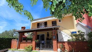 Una casa de dos pisos con balcón, fachada de ladrillo y un pequeño jardín con macetas.