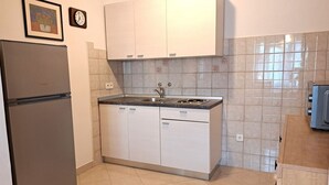 Una cocina compacta con armarios blancos, un refrigerador de acero inoxidable, un lavamanos y salpicadero de azulejos.