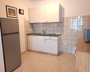 Eine kompakte Küche mit weißen Schränken, einem Edelstahlkühlschrank, einer Spüle und einer gefliesten Rückwand.