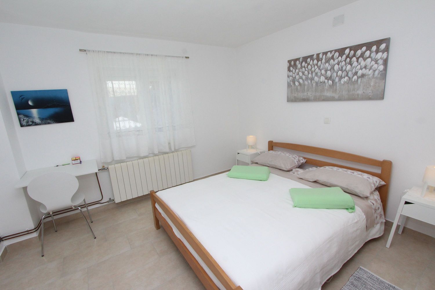 Un dormitorio con una cama, un escritorio, una silla, un radiador y un cuadro en la pared.