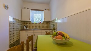 Una cocina pequeña con ventana, un lavamanos y una mesa con un cuenco de fruta.