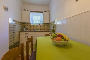 Eine kleine Küche mit Fenster, Spüle und Tisch mit Obstschüssel.