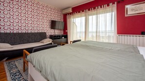 Un dormitorio con una cama grande, un sofá, un televisor y una ventana con cortinas.