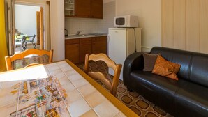 Ett kompakt bostadsutrymme med ett matbord, en svart lädersoffa, ett köksområde och ett litet kylskåp.
