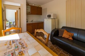 A compact living space with a dining table, a black leather sofa, a kitchen area, and a small refrigerator. - Dog-friendly apartment just 500 metres from the beach with Mediterranean terrace (Crikvenica)