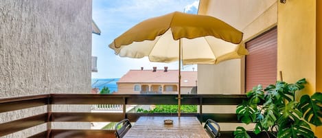 En balkon med et bord, stole, en stor parasol og en potteplante.