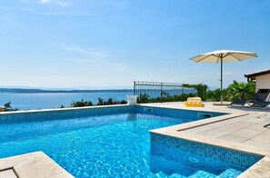 Una piscina con acqua cristallina, vista sul mare e area solarium con lettini e ombrellone.