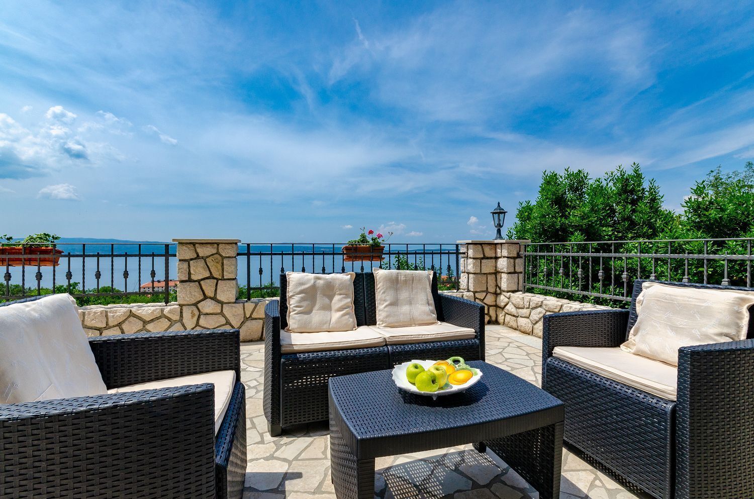 Una terrazza esterna con mobili in vimini, un muro in pietra e vista sul mare.