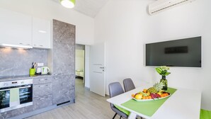Una cucina moderna con forno integrato, un'area pranzo con tavolo apparecchiato per due persone e una TV a schermo piatto montata a parete.