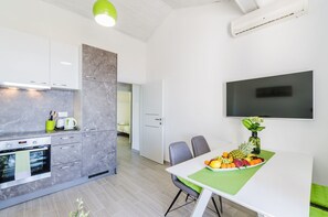 A modern kitchen with a built-in oven, a dining area with a table set for two, and a flat-screen TV mounted on the wall. - Light-filled apartment just 600 metres from the sandy beach with pool, gym, sea view (Crikvenica)