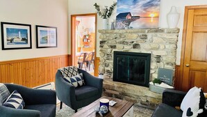 A cozy living room with a stone fireplace, two armchairs, a coffee table, and framed pictures on the wall. - Private 3BR Gem on 2.5 Wooded Acres- Close to All (Sister Bay)