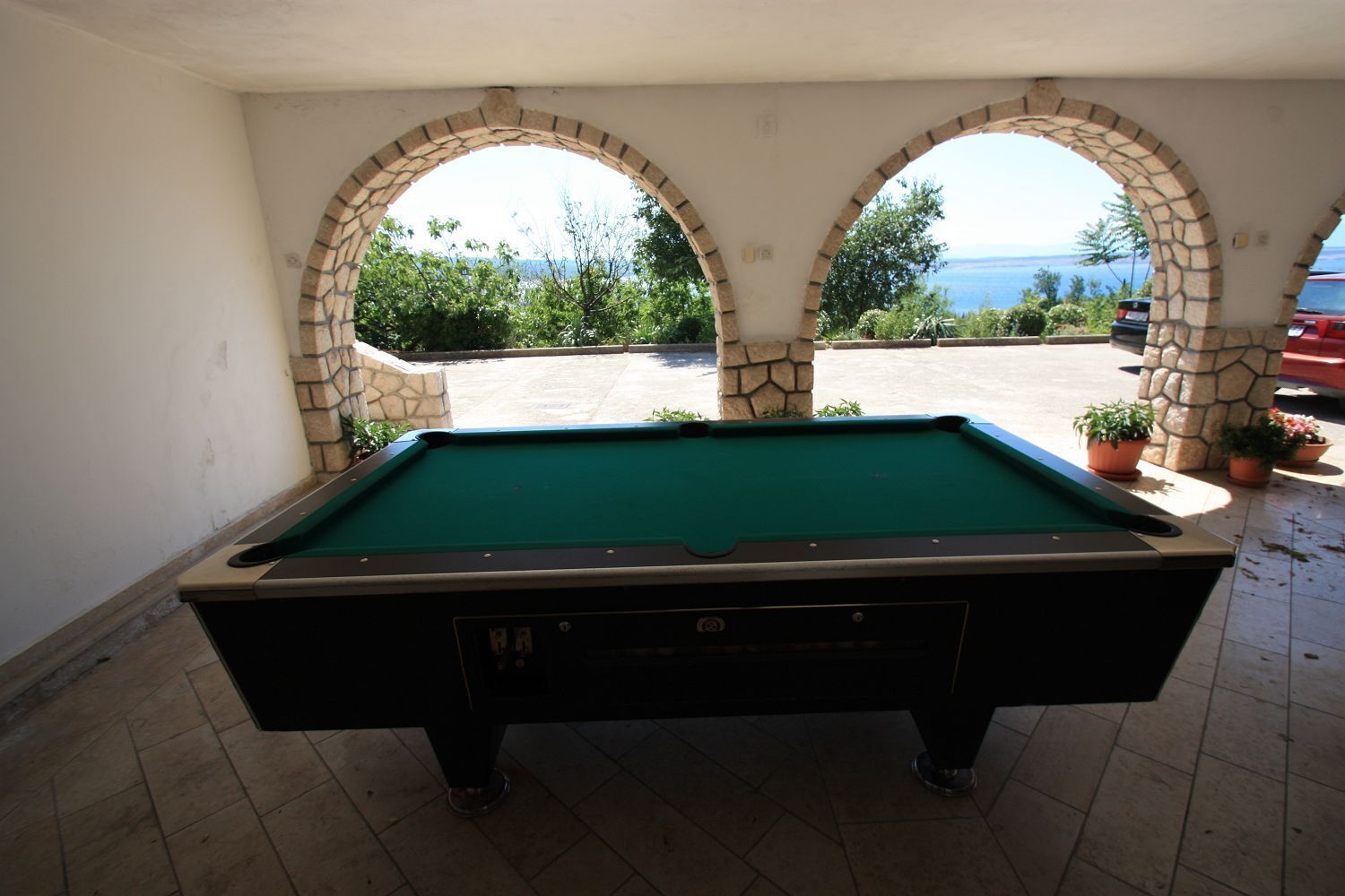 Een pooltafel in een overdekte ruimte met stenen bogen, uitzicht op zee, en potplanten.