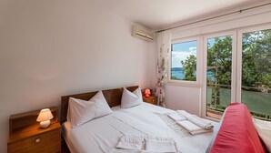 Una camera da letto con un letto grande, un comodino con una lampada, una finestra vista su vegetazione e acqua, e un condizionatore d'aria a parete.