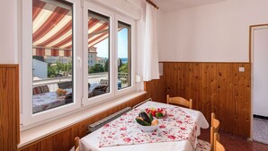 Zona pranzo con tavolo apparecchiato per due, una finestra con vista sugli edifici e pannelli di legno al muro.