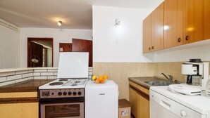 Una cocina compacta con estufa a gas, refrigerador, cafetera y muebles de madera.
