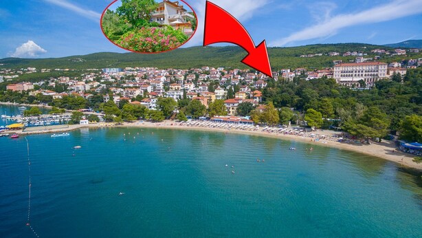 Vista aérea de un pueblo costero con playa, barcos y un edificio grande con tejado rojo.
