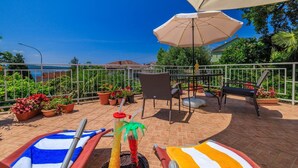 Un patio exterior con vista al mar, que incluye una mesa, sillas y una sombrilla.