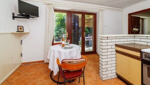 Cocina compacta con comedor, televisor montado en la pared y vista al jardín a través de la puerta.