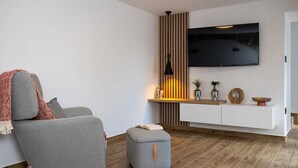 A modern living room with a grey sofa, a small ottoman, a wooden floor, a TV mounted on the wall, and a wooden panel with a vase and plants. - Mediterranean villa with private pool, sea view, dog-friendly, barbecue, private parking (Grižane)